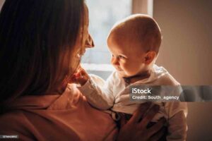 Two people, mother holding her baby son and playing at home.
