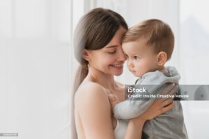 Cheerful young single mother hugging embracing little small son daughter baby newborn infant toddler indoors. Motherhood and childcare concept. Postnatal period